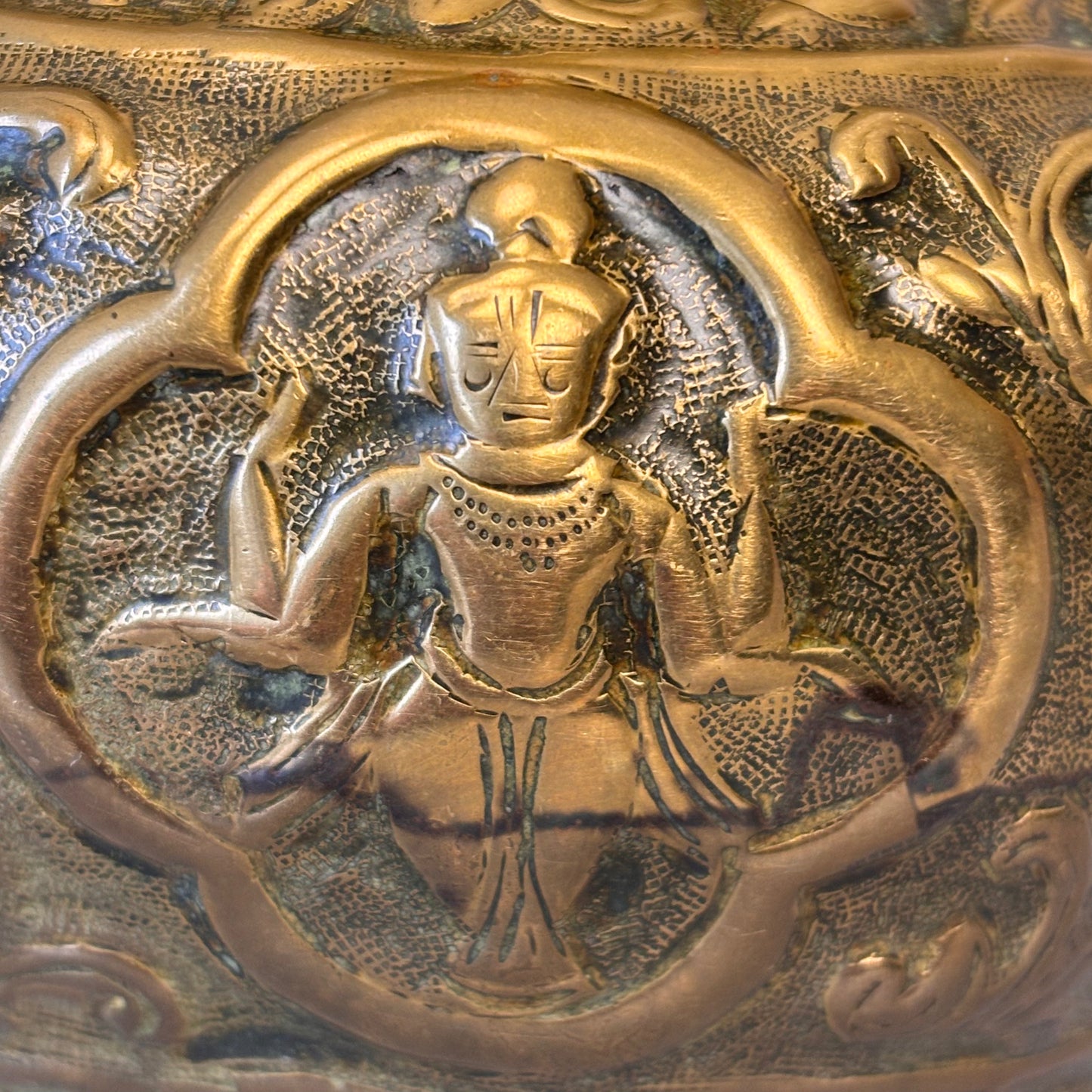Close-up of repoussé deity figure with punch-textured background
