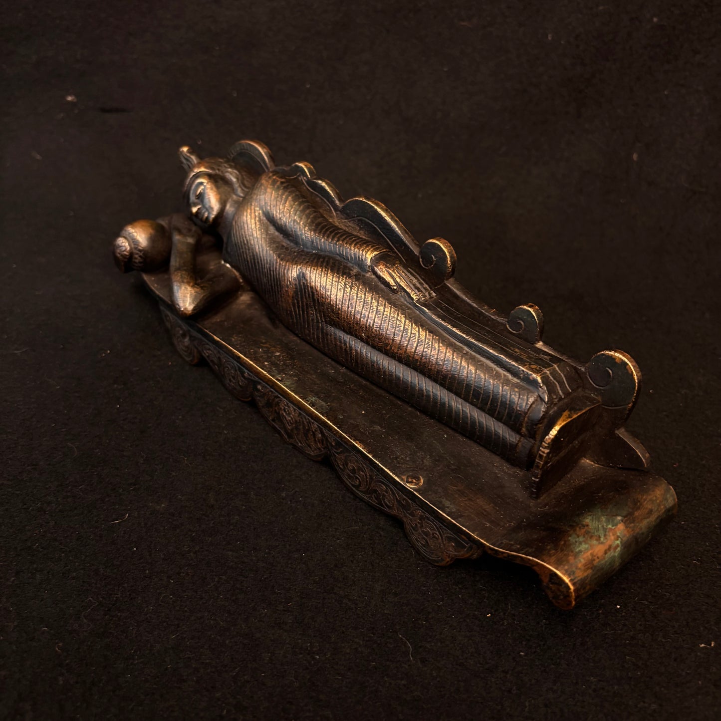 Side view of heavy bronze reclining Buddha showing robe detail and patina