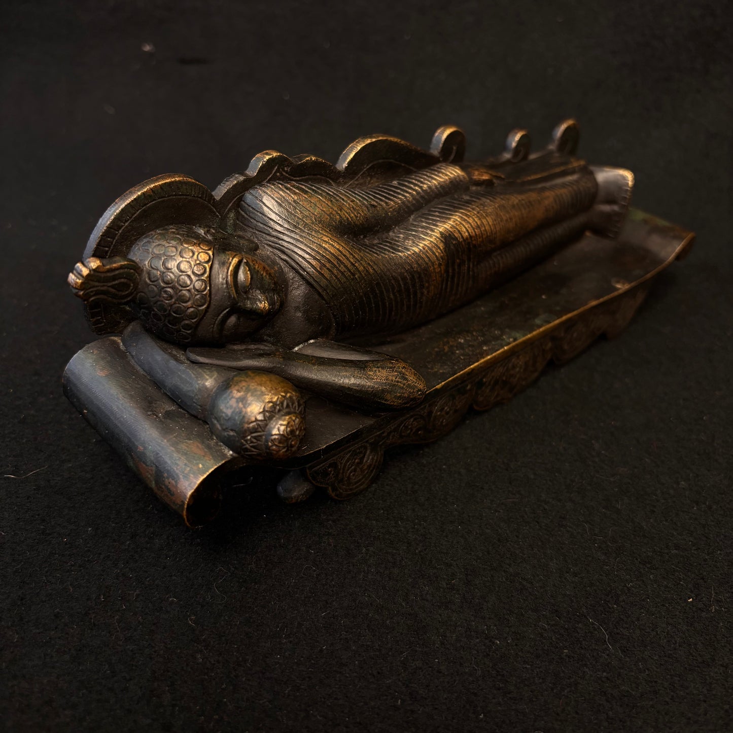 Side view of heavy bronze reclining Buddha showing robe detail and patina