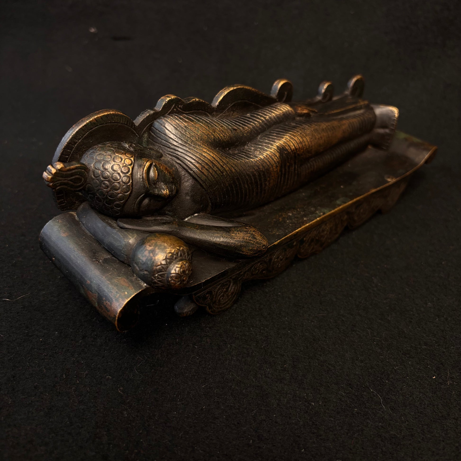 Side view of heavy bronze reclining Buddha showing robe detail and patina